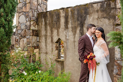 Bride and groom sharing a quiet embrace beside a weathered stone ruin wall