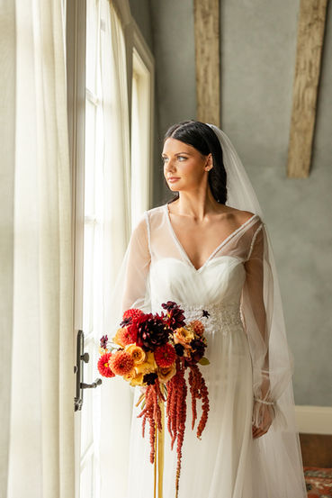 Bride in a sheer-sleeved gown holding a dramatic bouquet beside a rustic beamed wall