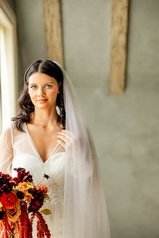 Bride portrait with a dramatic autumn bouquet against a plain timber-beamed wall