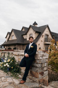 Groom leaning against a stone wall in front of the chateau's gabled rooftops