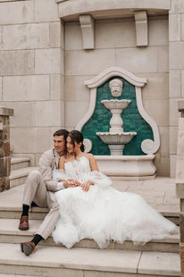 Bride and groom seated together on stone steps before a carved fountain