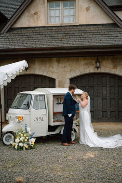 Bride and groom sharing a kiss beside a vintage mobile beverage cart