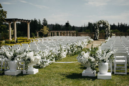 Rows of white ceremony chairs and floral urns set on the chateau's front lawn