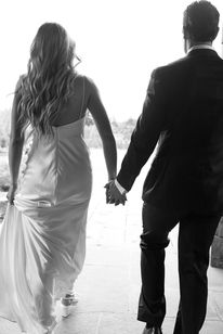 Bride and groom walking hand in hand into the light, seen from behind