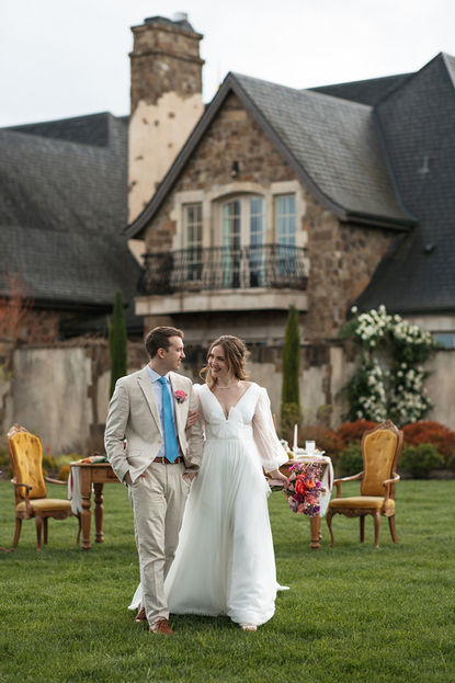 Bride and groom walking the chateau's front lawn as her gown billows in the wind